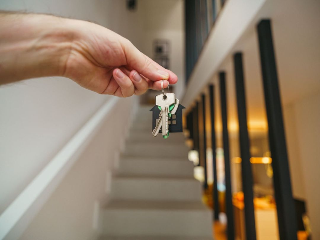 Hand übergibt einen Schlüsselbund im hellen Treppenhaus eines fertiggestellten Wohnhauses
