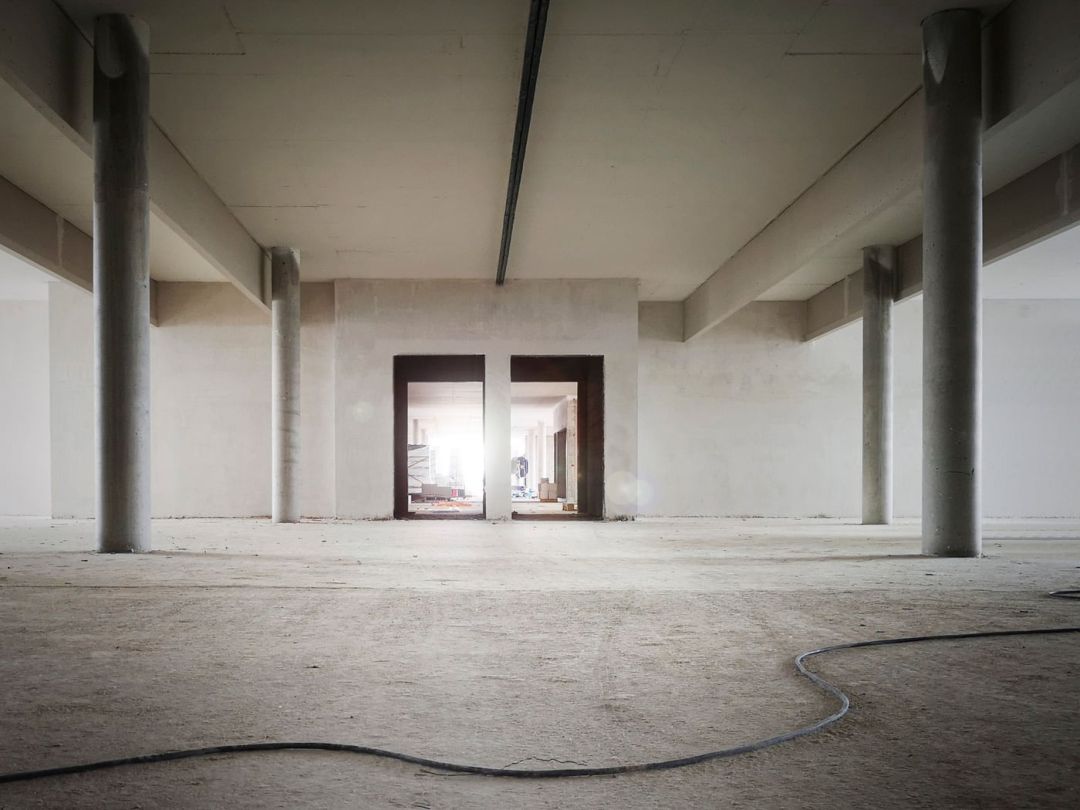 Fertige Betondecke und Bodenplatte eines Rohbaus, getragen von Stützen, im Hintergrund ein Türdurchbruch