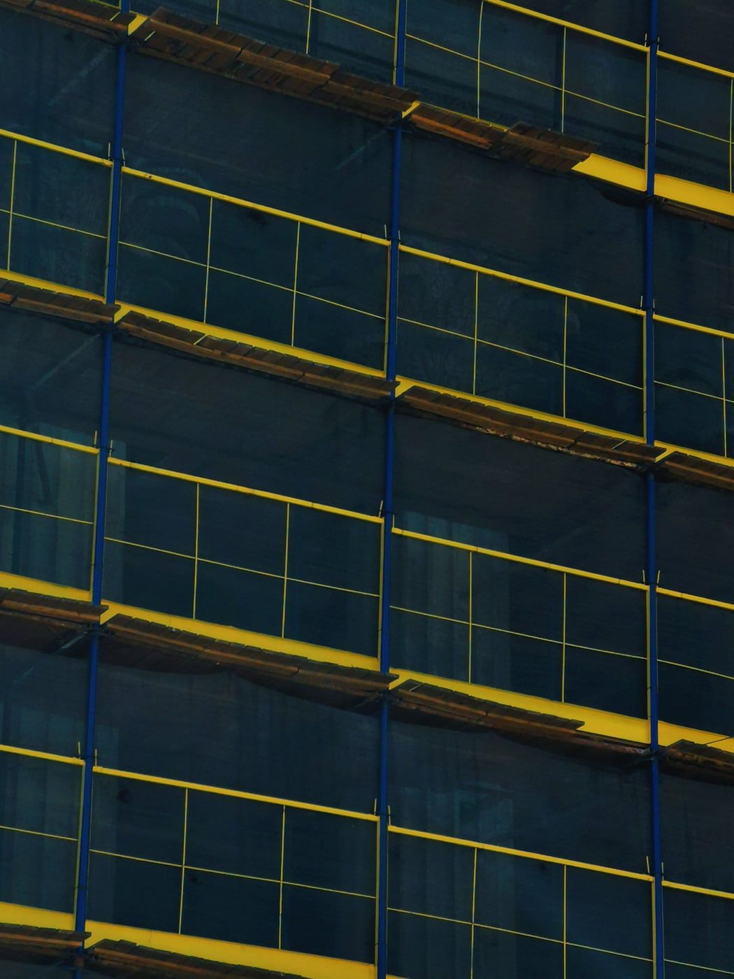 Gerüstlagen mit gelben Geländern und Bordbrettern vor einer mit dunklem Netz verhängten Fassade