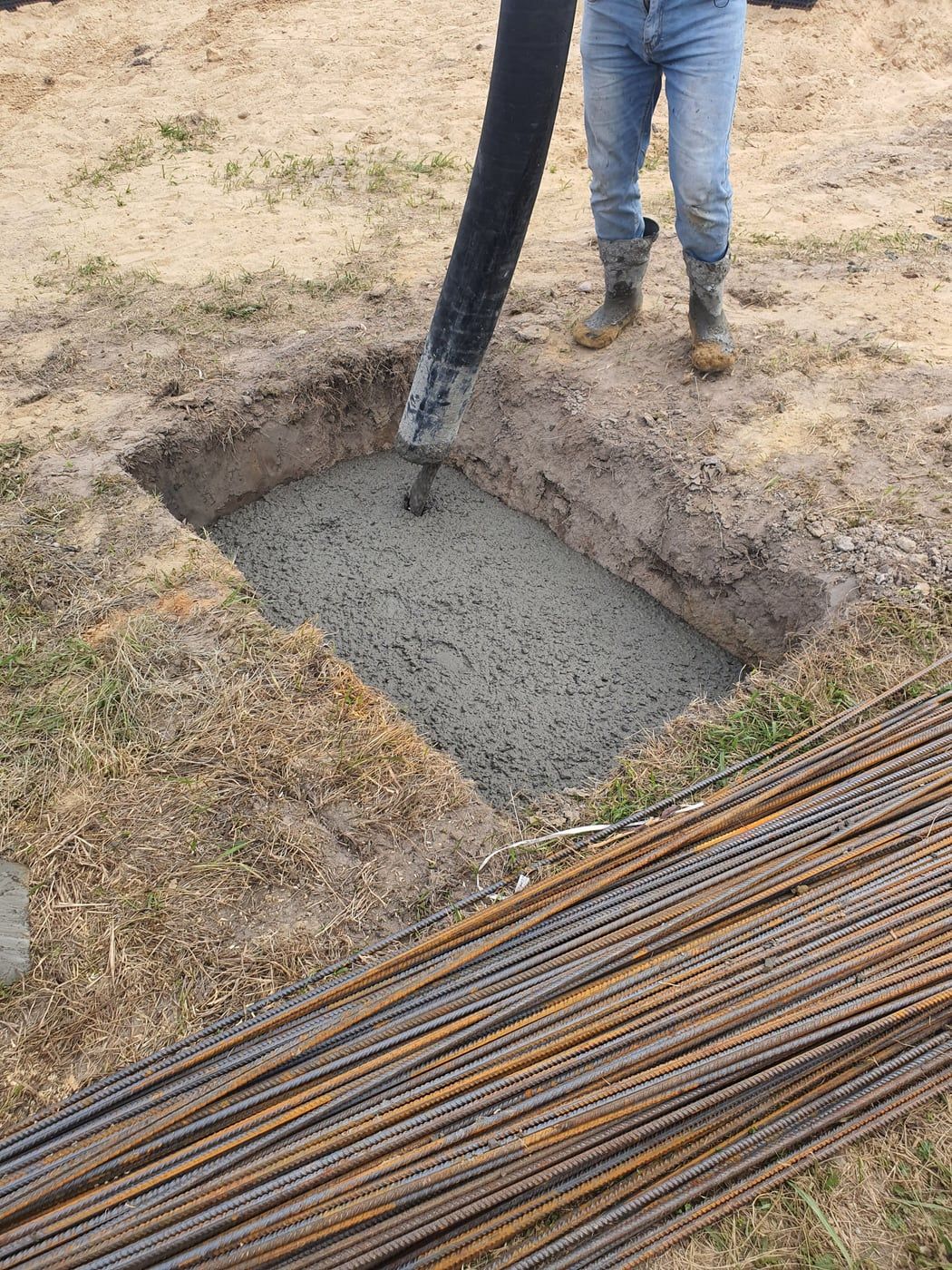 Ausgehobene Baugrube mit frisch eingebrachtem Beton, daneben liegen gebündelte Bewehrungsstäbe